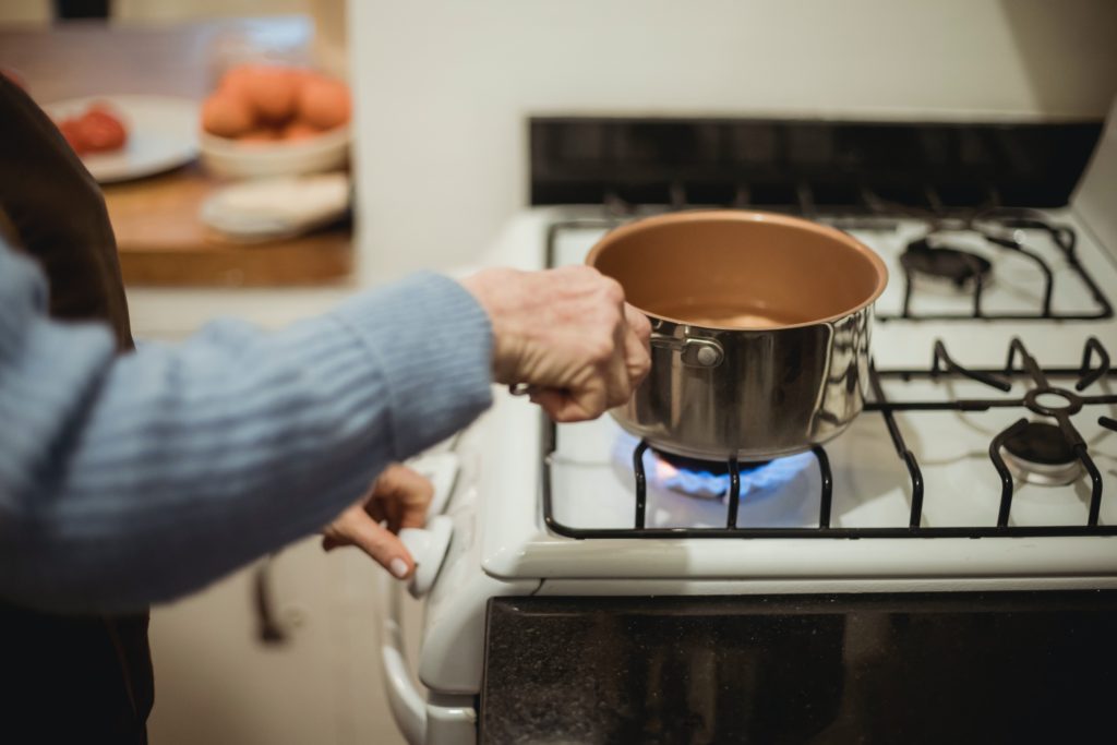 moça com uma panela na mão próximo de um fogão
