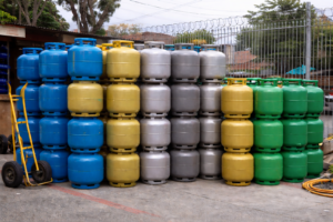 Botijões de gás azuis, amarelos, cinzas e verdes empilhados em depósito externo